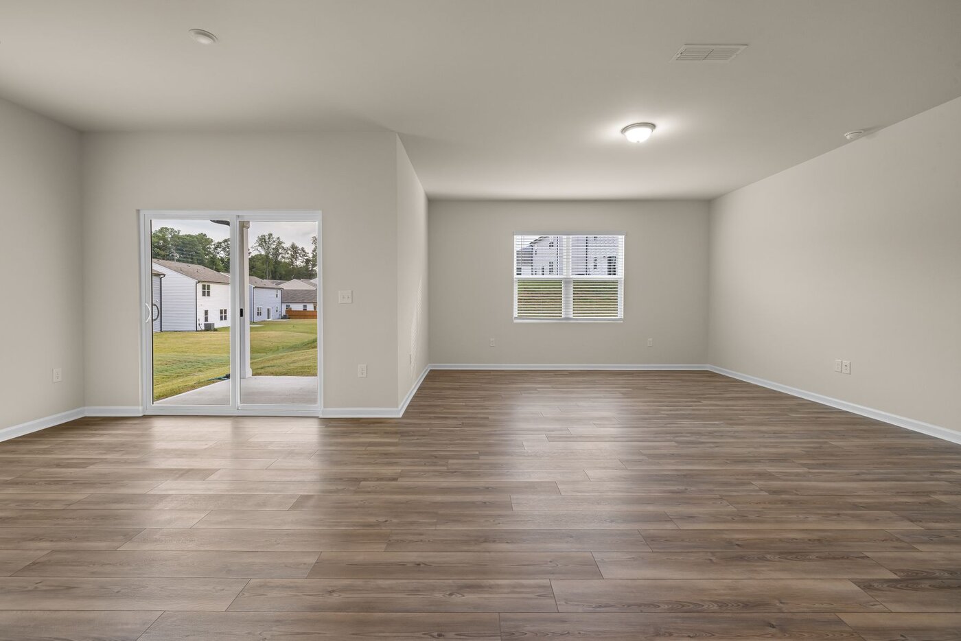 A bright unfurnished living room with wooden flooring and views towards a garden