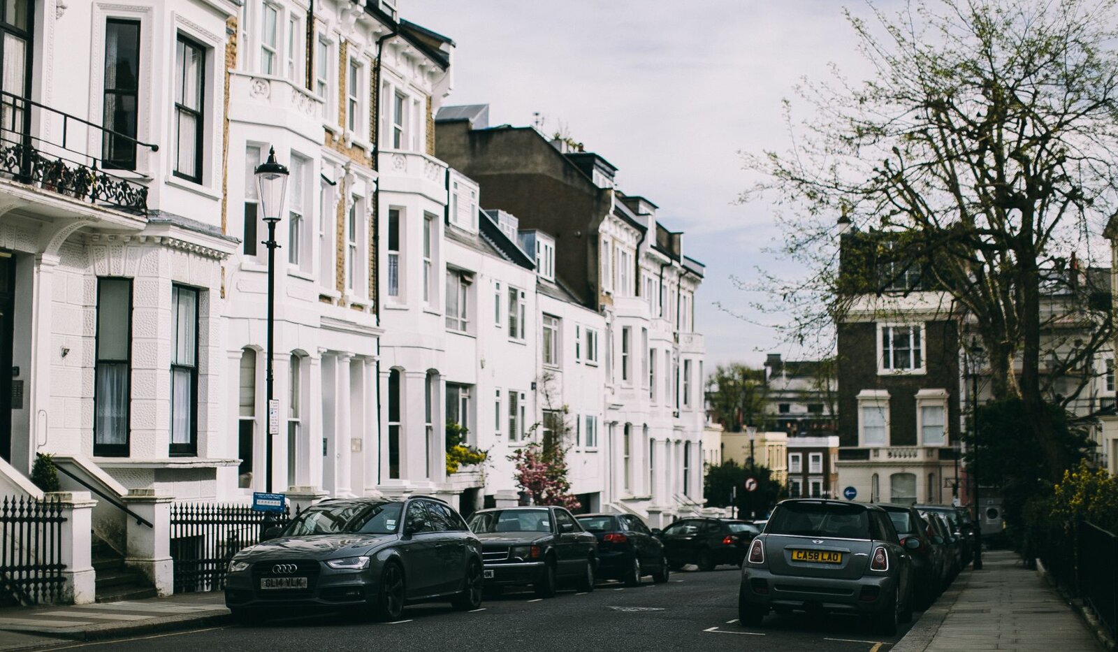A quiet British residential street lined with white terraced townhouses