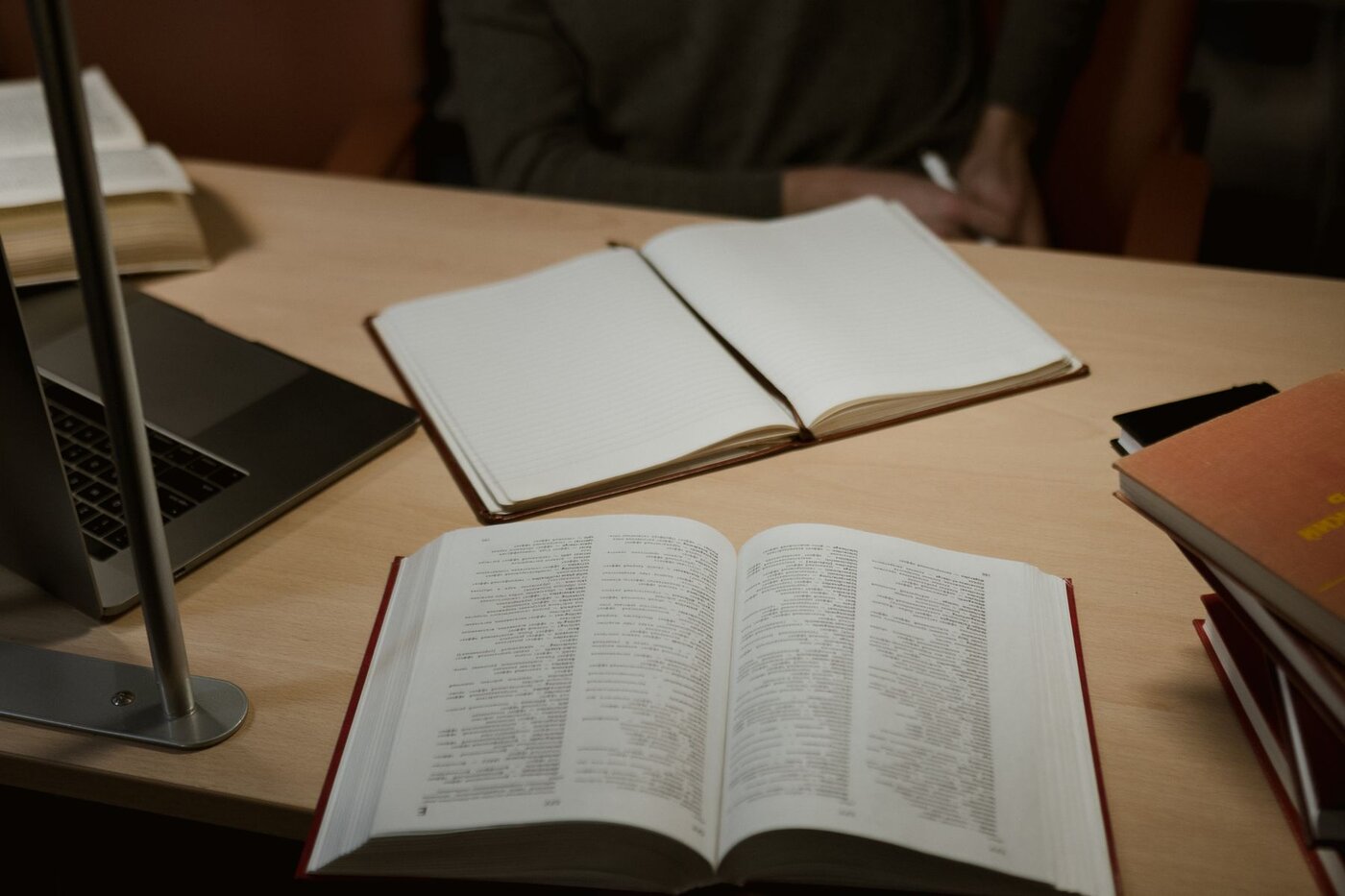 A laptop, open notebook and reference books arranged on a desk for an illustrative research session