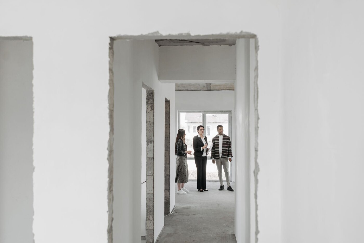 Prospective buyers and an agent viewing a property through a series of unfinished doorways